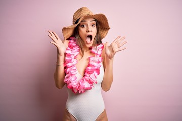 Young beautiful brunette woman on vacation wearing swimsuit and Hawaiian flowers lei celebrating...