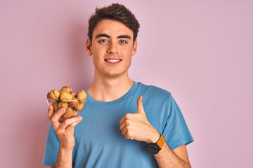 Teenager boy holding bunch of natural walnuts over pink isolated background happy with big smile doing ok sign, thumb up with fingers, excellent sign