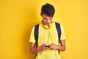 Teenager boy wearing headphones and using smartphone over isolated background scared in shock with a surprise face, afraid and excited with fear expression