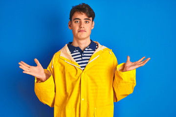 Teenager fisherman boy wearing yellow raincoat over isolated background clueless and confused...