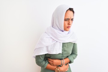 Young beautiful Arab woman wearing traditional Muslim hijab over isolated background with hand on stomach because nausea, painful disease feeling unwell. Ache concept.