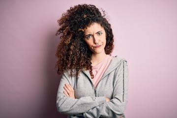 Young beautiful brunette sportswoman with curly hair and piercing wearing sportswear skeptic and...