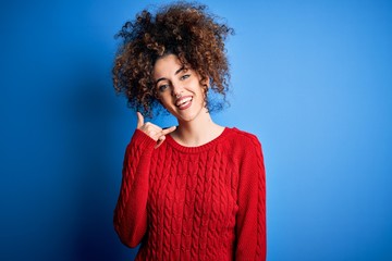 Fototapeta na wymiar Young beautiful woman with curly hair and piercing wearing casual red sweater smiling doing phone gesture with hand and fingers like talking on the telephone. Communicating concepts.
