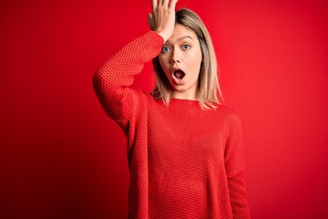 Young beautiful blonde woman wearing casual sweater over red isolated background surprised with...