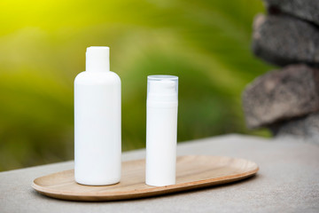 Fototapeta na wymiar White empty tube of skincare bottle on bamboo plate over tropical background. Skincare spray tube for spa relax.