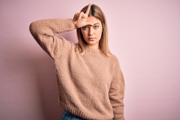 Young beautiful blonde woman wearing winter wool sweater over pink isolated background making fun of people with fingers on forehead doing loser gesture mocking and insulting.