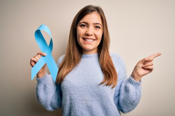 Young blonde woman holding prostate cancer awareness campaing blue ribbon very happy pointing with...
