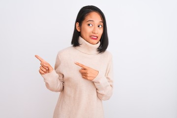 Young chinese woman wearing turtleneck sweater standing over isolated white background Pointing aside worried and nervous with both hands, concerned and surprised expression