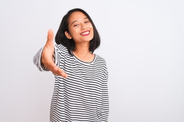 Young chinese woman wearing striped t-shirt standing over isolated white background smiling friendly offering handshake as greeting and welcoming. Successful business.