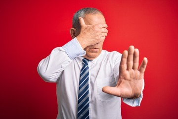 Senior handsome businessman wearing elegant tie standing over isolated red background covering eyes with hands and doing stop gesture with sad and fear expression. Embarrassed and negative concept.