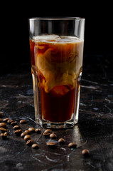 Iced coffee in a glass with pouring milk in black background