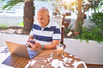 Senior handsome man smiling happy and confident. Sitting using laptop and smartphone at terrace