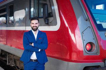 Portrait of young bearded train driver in blue uniform proudly standing in front of modern subway...