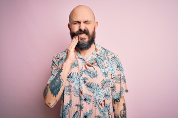 Handsome bald man with beard and tattoo wearing casual floral shirt over pink background touching mouth with hand with painful expression because of toothache or dental illness on teeth. Dentist