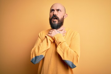 Obraz premium Handsome bald man with beard wearing casual sweater standing over yellow background shouting and suffocate because painful strangle. Health problem. Asphyxiate and suicide concept.