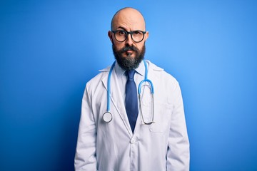 Handsome bald doctor man with beard wearing glasses and stethoscope over blue background skeptic and nervous, frowning upset because of problem. Negative person.