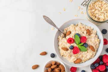Bowl of oatmeal porridge with fresh berries, almonds and mint with a spoon for healthy diet breakfast on white table