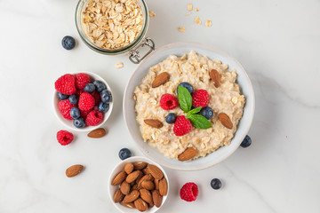 Oatmeal porridge in a bowl with fresh berries, nuts and mint on white background for healthy diet breakfast.