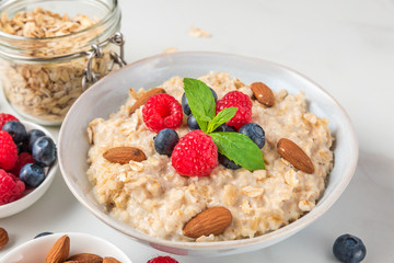 Oatmeal porridge in a bowl with fresh berries, nuts and mint on white background for healthy diet breakfast