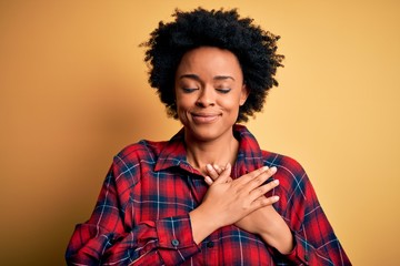 Young beautiful African American afro woman with curly hair wearing casual shirt smiling with hands on chest with closed eyes and grateful gesture on face. Health concept.