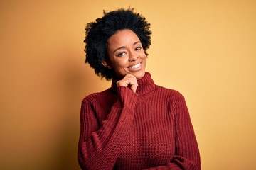 Fototapeta na wymiar Young beautiful African American afro woman with curly hair wearing casual turtleneck sweater looking confident at the camera smiling with crossed arms and hand raised on chin. Thinking positive.