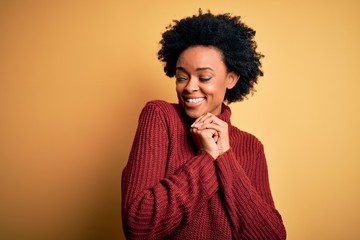 Fototapeta na wymiar Young beautiful African American afro woman with curly hair wearing casual turtleneck sweater laughing nervous and excited with hands on chin looking to the side