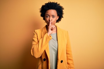 Fototapeta na wymiar Young beautiful African American afro businesswoman with curly hair wearing yellow jacket asking to be quiet with finger on lips. Silence and secret concept.