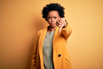 Young beautiful African American afro businesswoman with curly hair wearing yellow jacket looking unhappy and angry showing rejection and negative with thumbs down gesture. Bad expression.