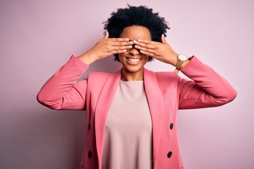 Young beautiful African American afro businesswoman with curly hair wearing pink jacket covering eyes with hands smiling cheerful and funny. Blind concept.