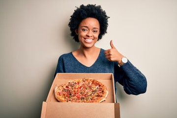 Young African American afro woman with curly hair holding delivery box with Italian pizza happy...