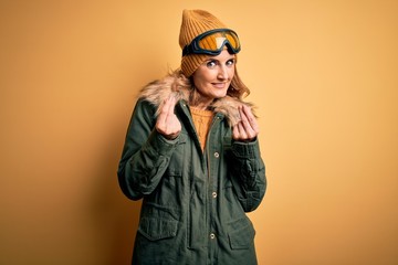 Middle age beautiful blonde skier woman wearing snow sportwear and ski goggles doing money gesture with hands, asking for salary payment, millionaire business
