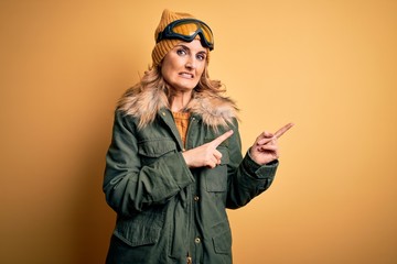 Middle age beautiful blonde skier woman wearing snow sportwear and ski goggles Pointing aside worried and nervous with both hands, concerned and surprised expression