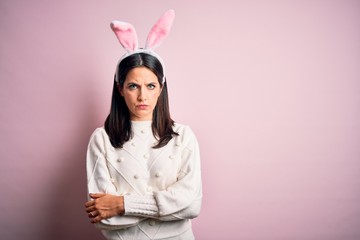 Young caucasian woman wearing cute easter rabbit ears over pink isolated background skeptic and nervous, disapproving expression on face with crossed arms. Negative person.