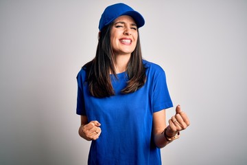 Young delivery woman with blue eyes wearing cap standing over blue background very happy and excited doing winner gesture with arms raised, smiling and screaming for success. Celebration concept.