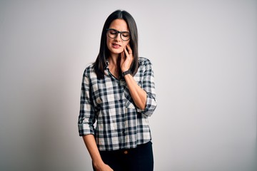 Young brunette woman with blue eyes wearing casual shirt and glasses over white background touching mouth with hand with painful expression because of toothache or dental illness on teeth. Dentist