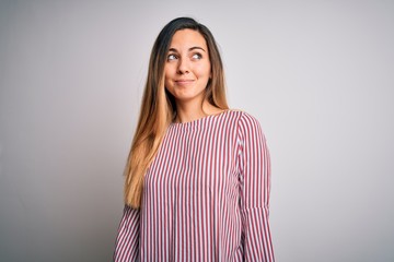 Young beautiful blonde woman with blue eyes wearing stiped t-shirt over white background smiling looking to the side and staring away thinking.