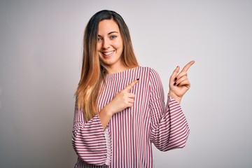 Young beautiful blonde woman with blue eyes wearing stiped t-shirt over white background smiling and looking at the camera pointing with two hands and fingers to the side.