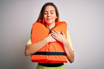 Young beautiful blonde woman with blue eyes wearing orange lifejacket over white background smiling...