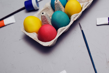 Happy easter. Colored eggs on gray concrete. Flowering, fur-seal willow, on an abstract gray background. Multicolored paints, brushes, watercolor. Space for text, empty space. Easter.