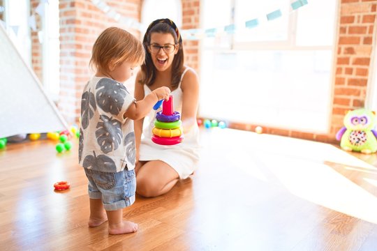 Beautiful teacher and toddler building pyramid using hoops around lots of toys at kindergarten