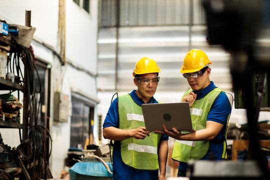 Two Asian Maintenance Engineers Discuss Inspect Relay Checking Information And Protection System On A Tablet Computer In A Factory. They Work A Heavy Industry Manufacturing Factory.