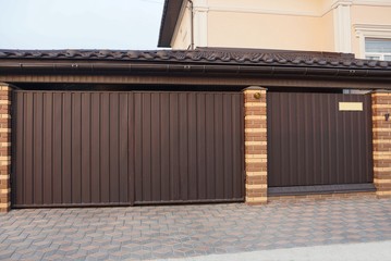 a large brown gate and a metal door and part of the fence on the sidewalk