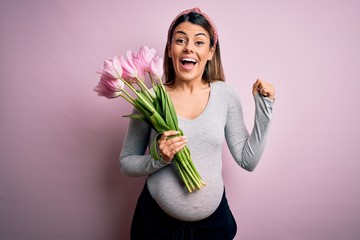 Young beautiful brunette woman pregnant expecting baby holding bouquet of tulips screaming proud and celebrating victory and success very excited, cheering emotion