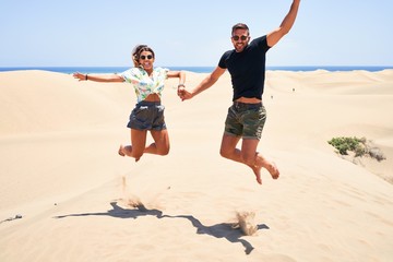 Young beautiful couple smiling happy and confident. Jumping with smile on face at the beach