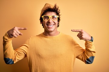 Young handsome man wearing casual t-shirt and glasses over isolated yellow background looking...