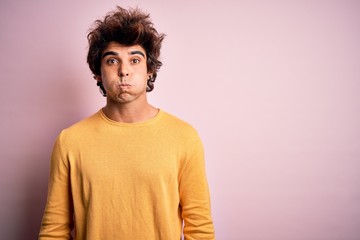 Young handsome man wearing yellow casual t-shirt standing over isolated pink background puffing cheeks with funny face. Mouth inflated with air, crazy expression.