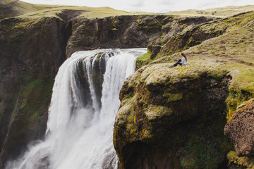 Woman sitting on edge with breathtaking view of Fagrifoss waterfall in Iceland. Lakagigar landmark...
