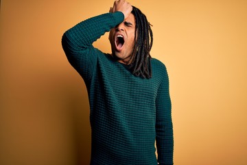 Young handsome african american afro man with dreadlocks wearing green casual sweater surprised...