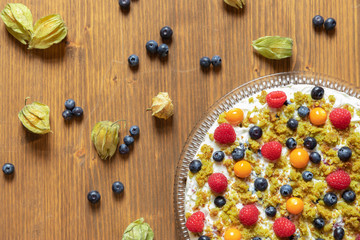 Moostorte aus grünem Biscuit mit Quark, Sahne, Früchte, Blaubeere, Himbeere, Physalis auf Holz