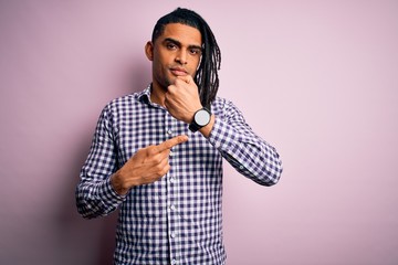 Young handsome african american afro man with dreadlocks wearing casual shirt In hurry pointing to watch time, impatience, looking at the camera with relaxed expression